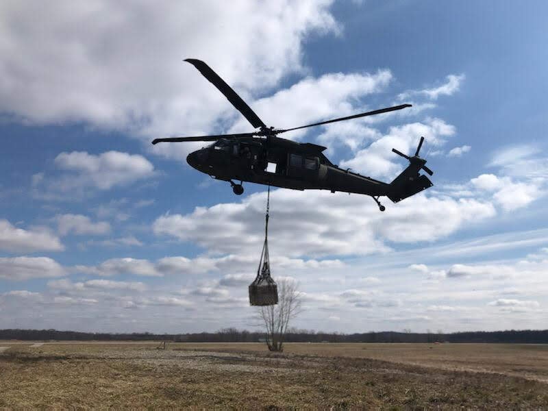 Military helicopter performing a field airlift operation with suspended cargo